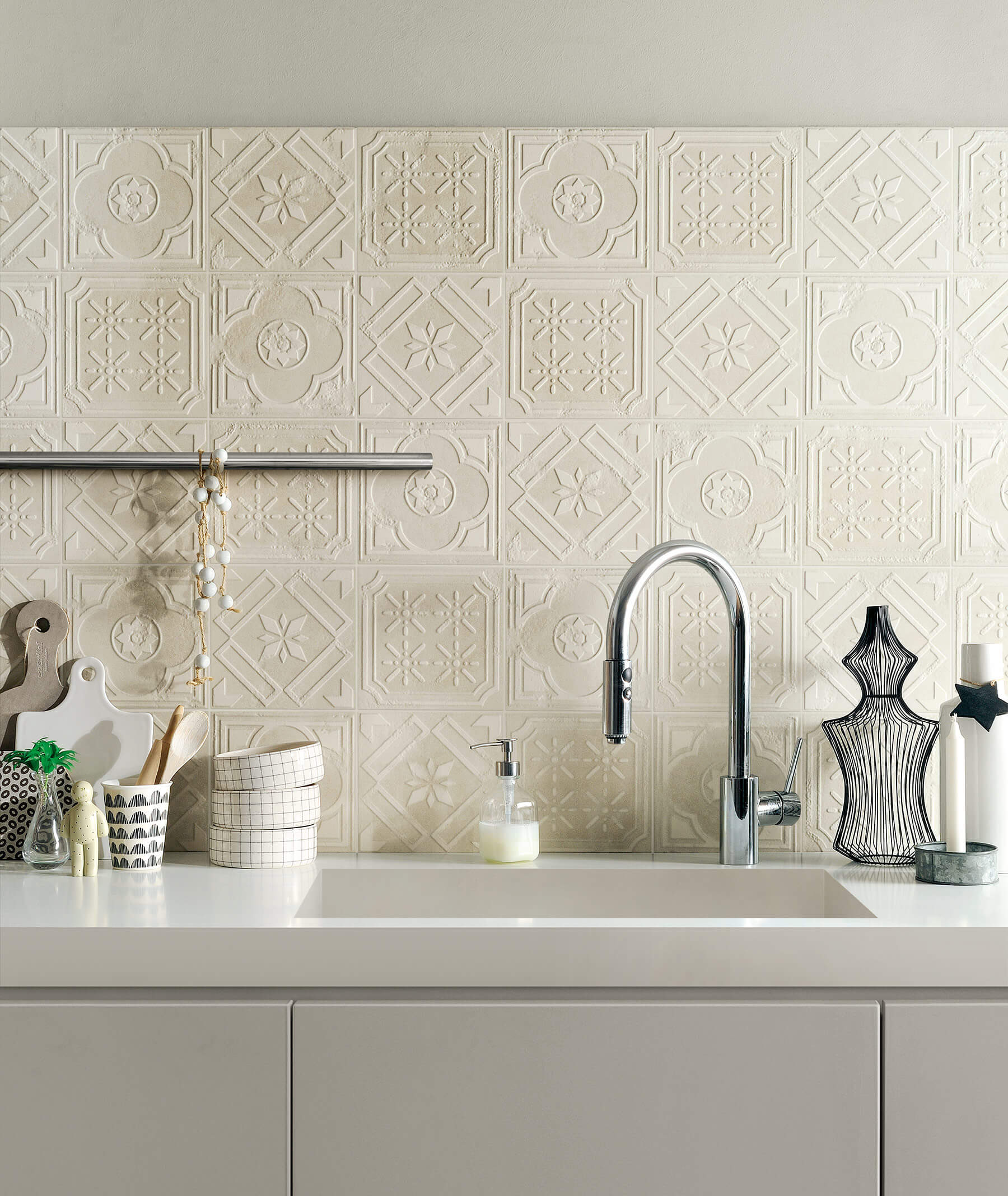 Close up of kitchen splashback using tiles with pattern that looks like pressed tin. Tiles are a soft cream colour.