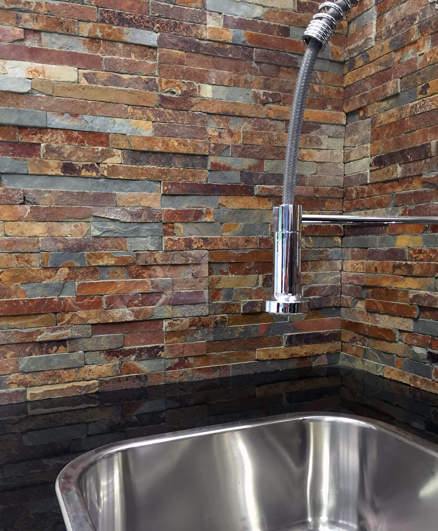 Close up of wall behind laundry sink showing tiles that look like stacked stone.