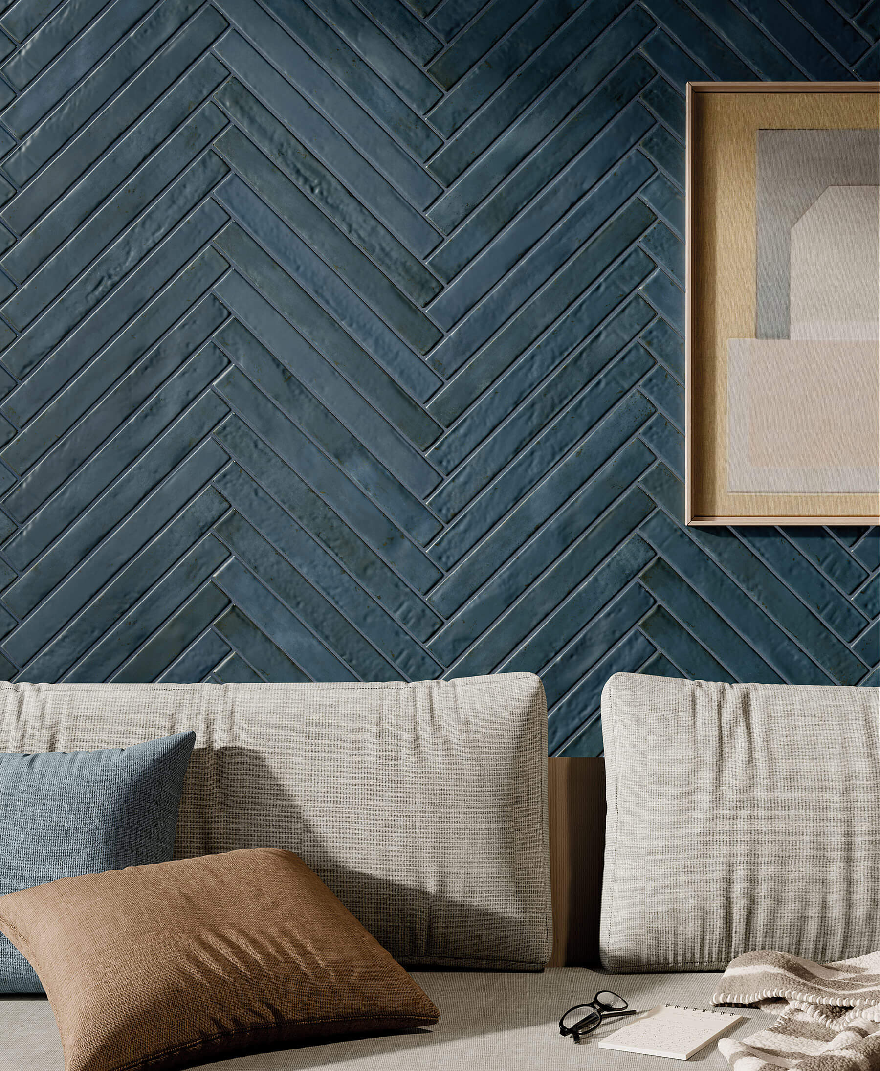 Close up of lounge wall with grey couch and feature wall of denim blue subway tiles laid in herringbone pattern.