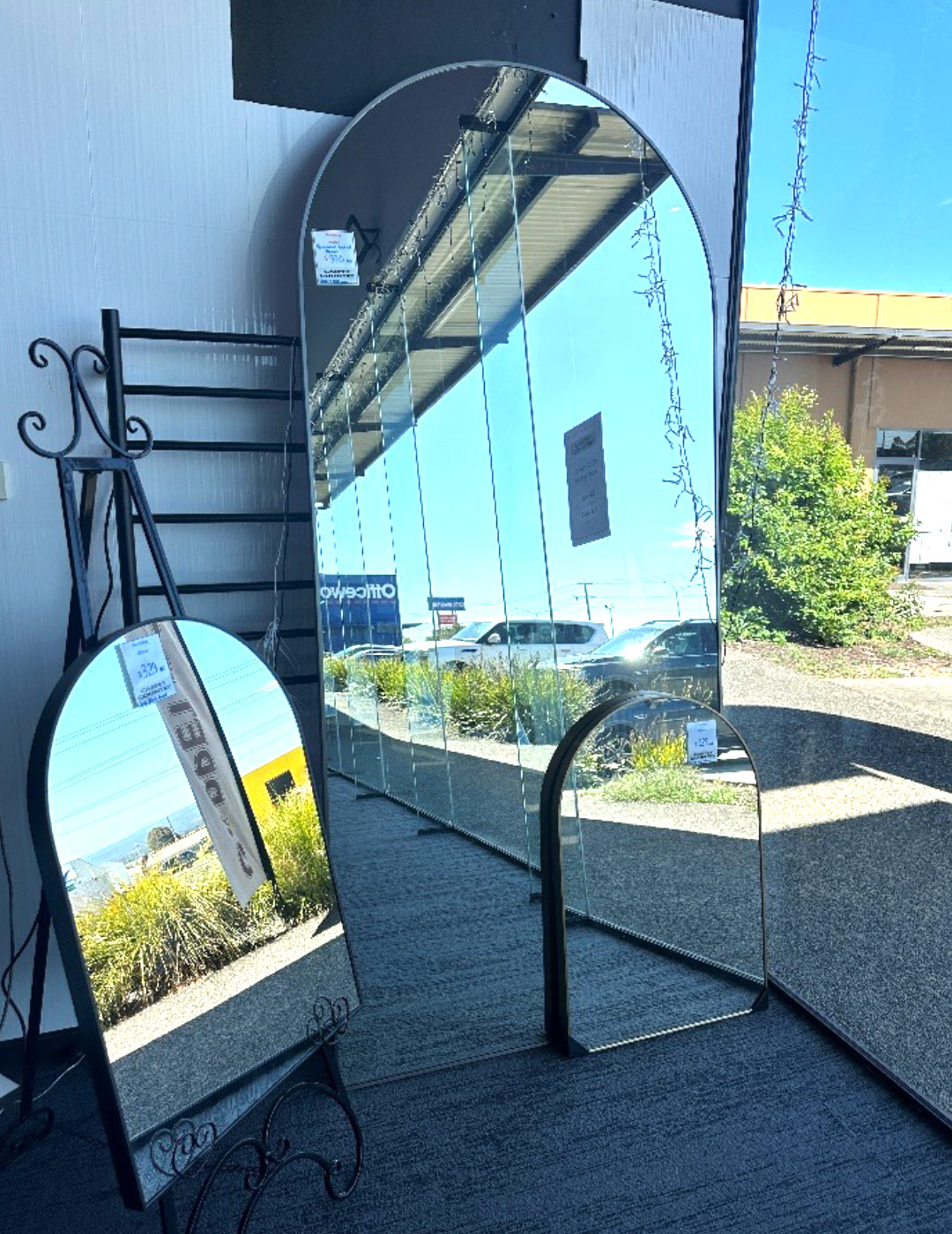 Selection of sizes of mirrors with rounded tops leaning against a wall in a store.