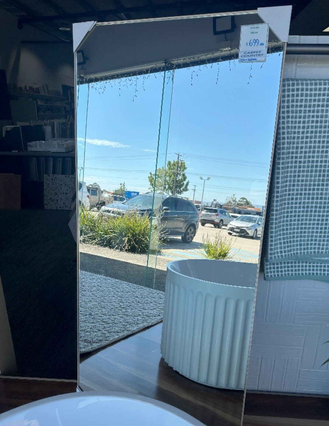 Tall rectangle mirror on display in a store, reflecting the carpark outside.