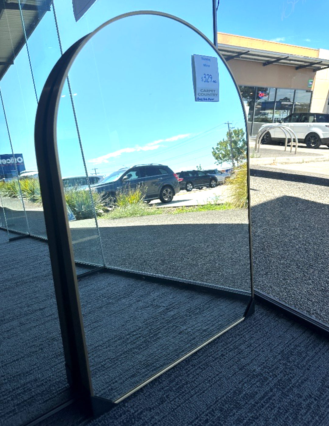Small mirror with rounded top leaning against a wall in a store.
