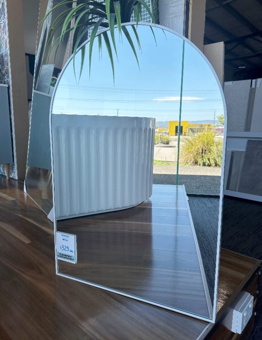Small mirror with rounded top leaning against a wall in a store.