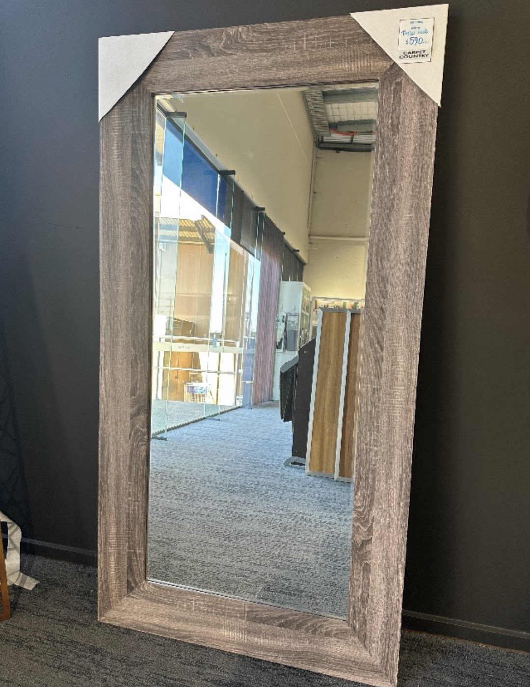 Rectangle mirror with thick wooden frame in a coastal style, leaning against a wall in a store.