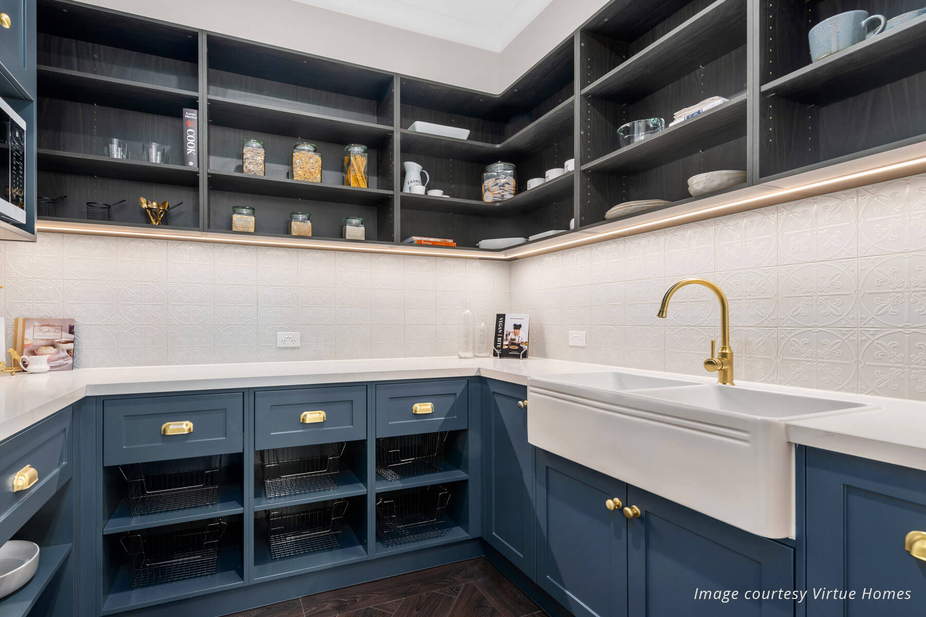 Farmhouse style butlers pantry with charcoal blue cabinets, white benchtops and open upper shelving. Gold tap and fittings, and detailed white backsplash tiles.