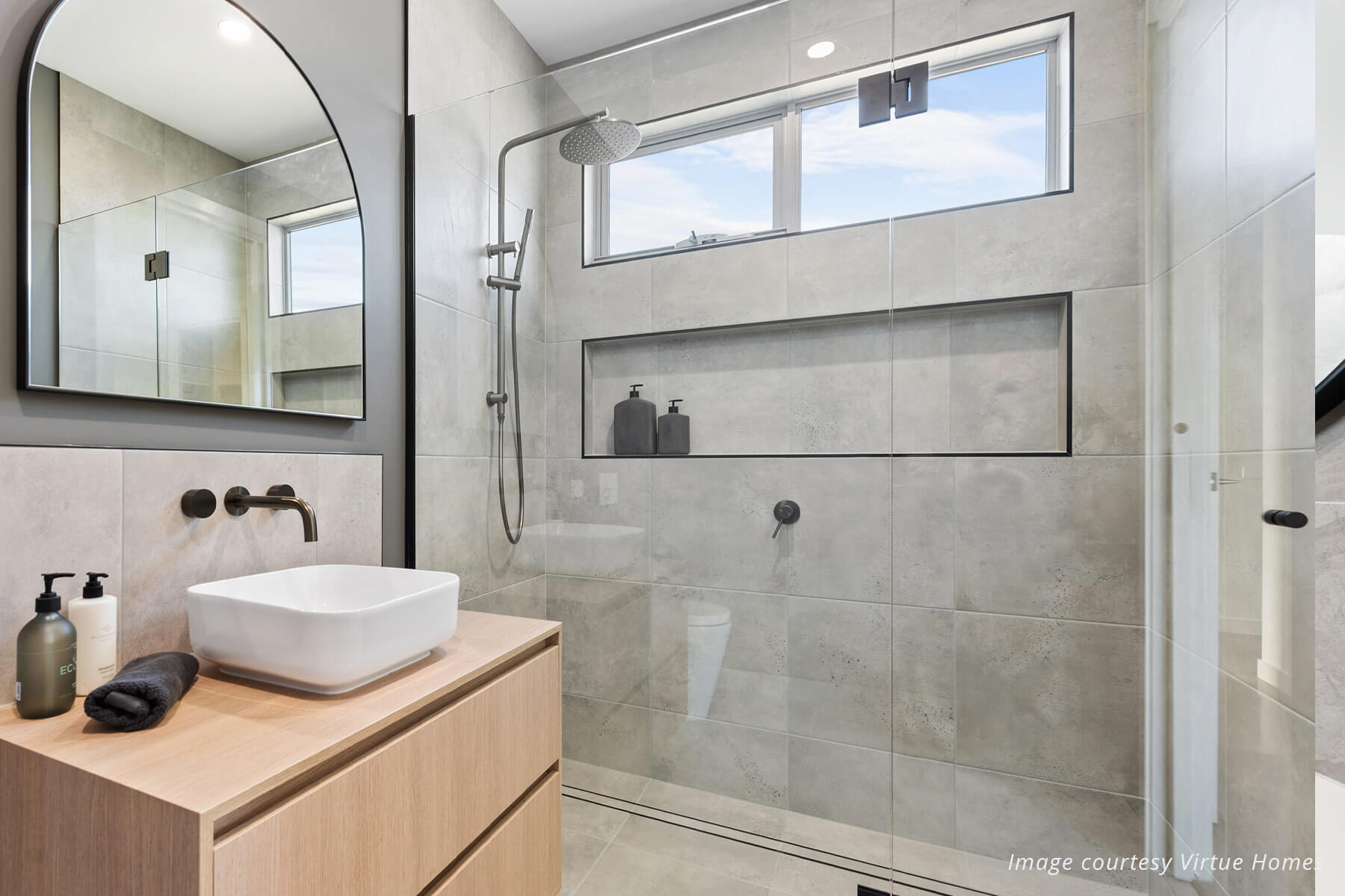 Modern bathroom with timber vanity and grey tiles in a large shower. Black tapware.