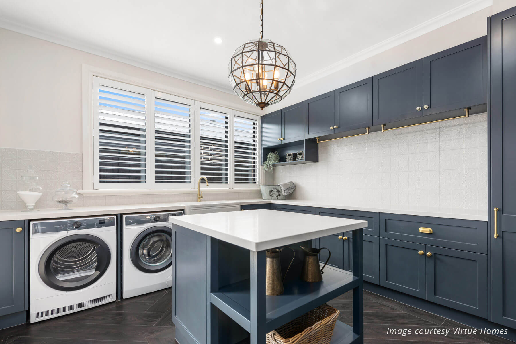 Large farmhouse style laundry with charcoal blue cabinets, white stone benchtops, white walls and central glass light.
