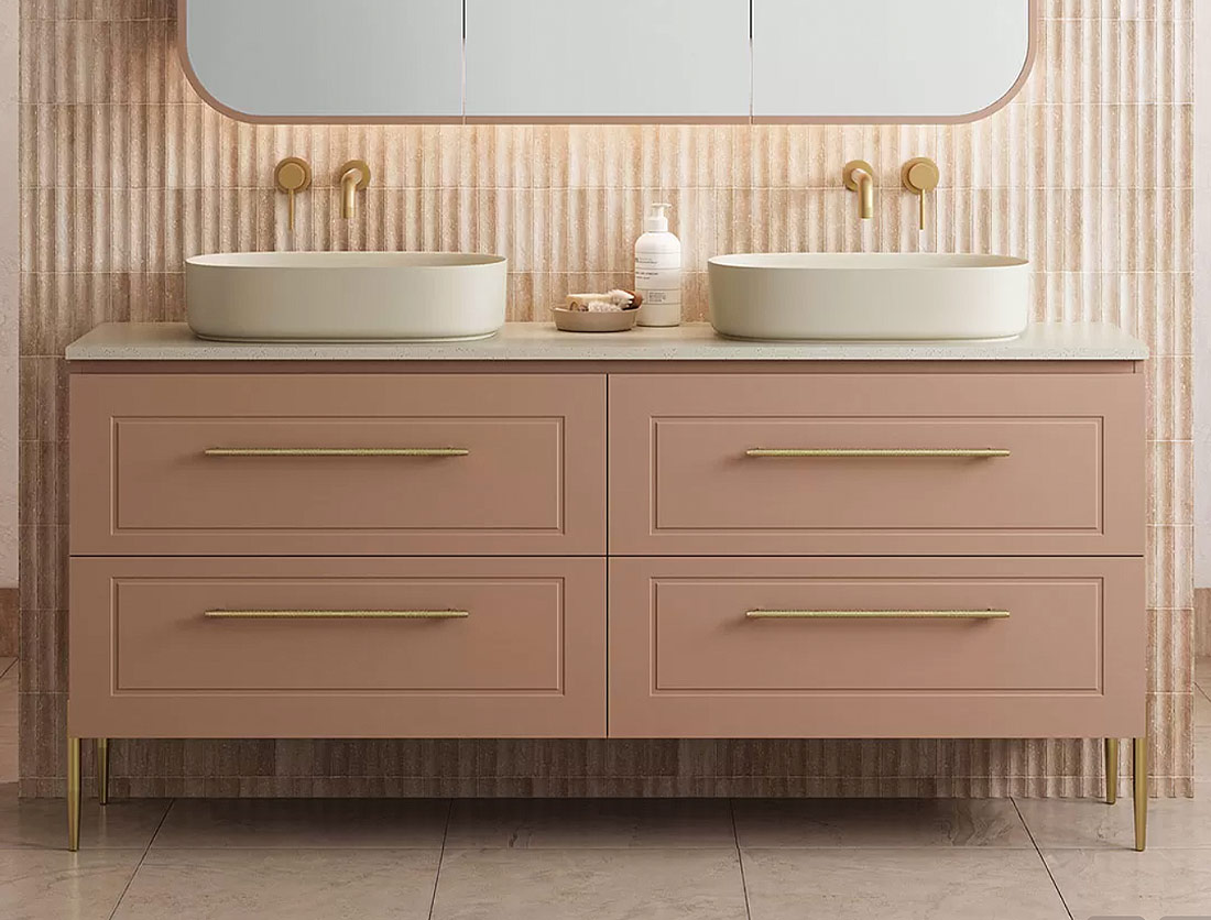 Close up of peach colour double vanity, white basins, gold tapware and sand colour subway tiles as the feature splashack.