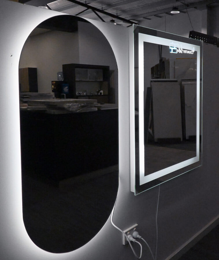 Two mirrors with back-lite features on a display wall. Left mirror is tall with rounded top and bottom, and right mirror is square.