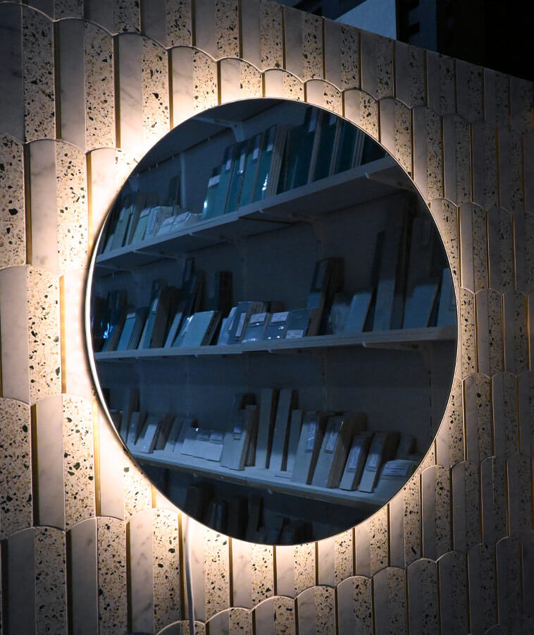 Round mirror with light behind it on a tile wall, shown in a display in a store.
