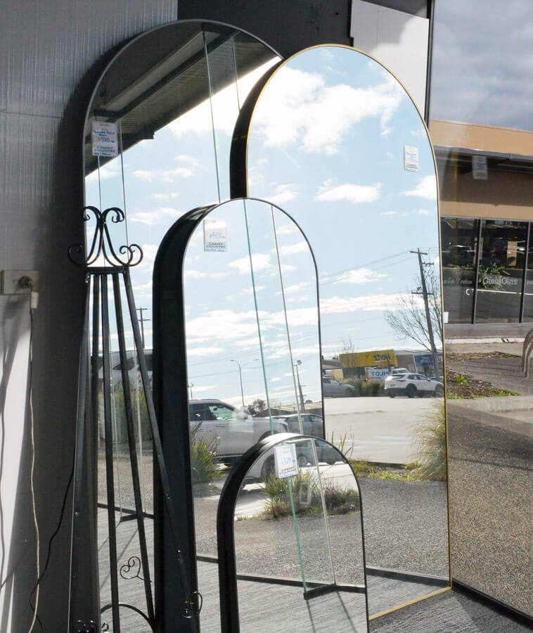 Tall, medium and short mirrors with rounded tops are stacked together in a window leaning against a wall.