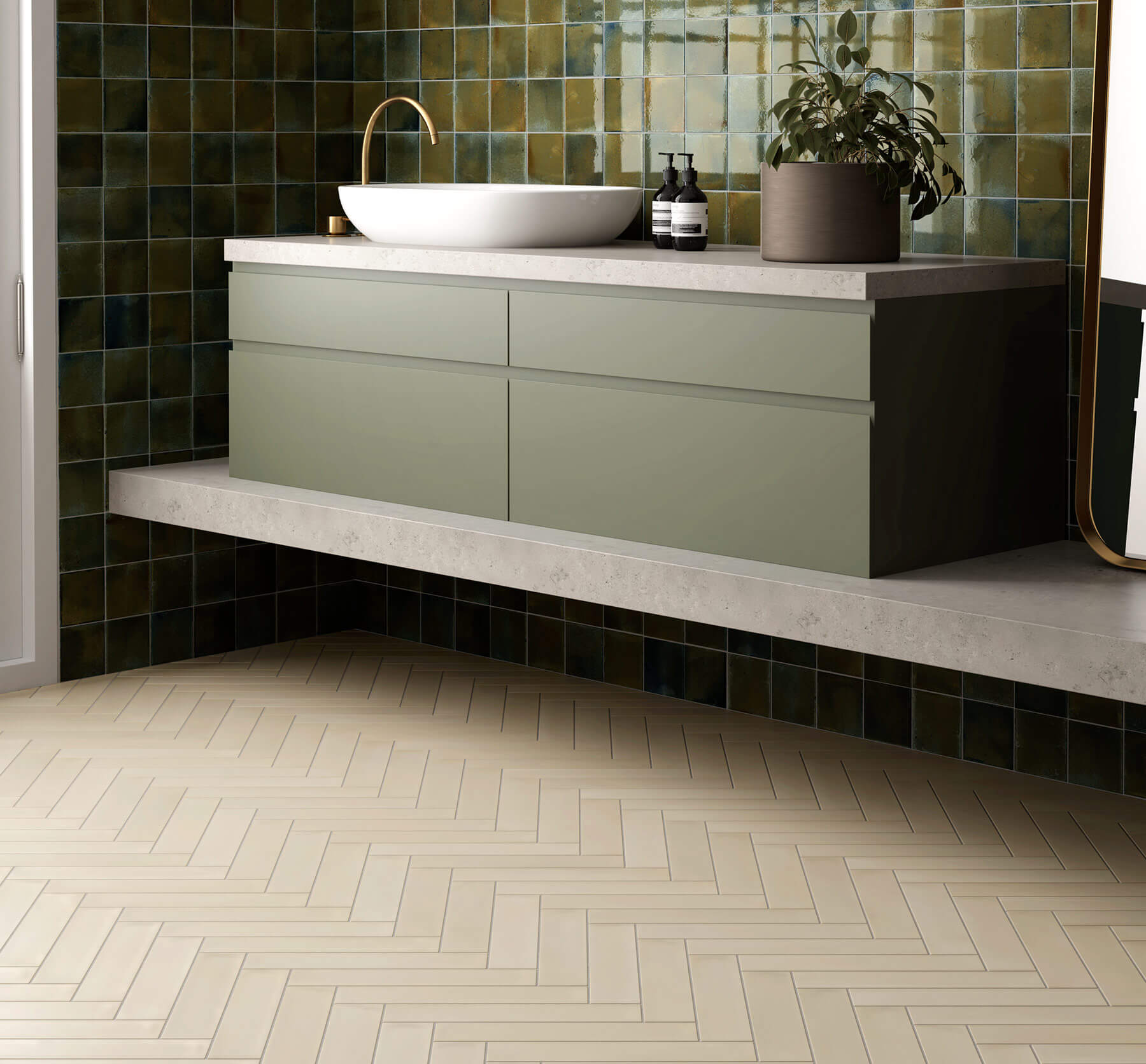 Modern bathroom with subway tile floor laid in a herringbone pattern in a soft tan colour, concrete bench with sage green vanity sitting on it. A white basin with gold tapware and feature wall with small sqaure green tiles.
