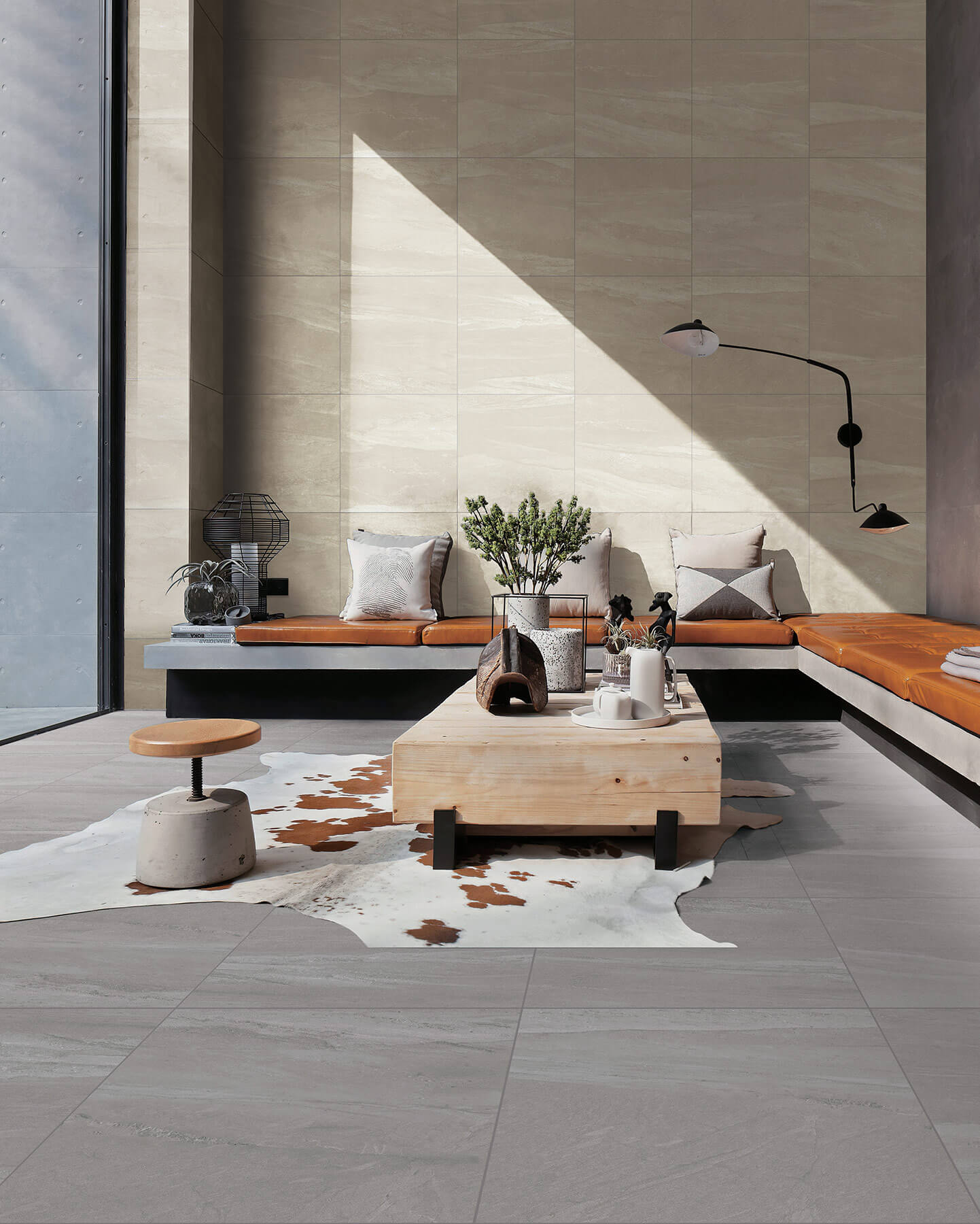 Contemporary living room with large square sandstone colour tiles as a feature wall, large square concrete tiles on the floor, and a modern built in couch and timber coffee table.