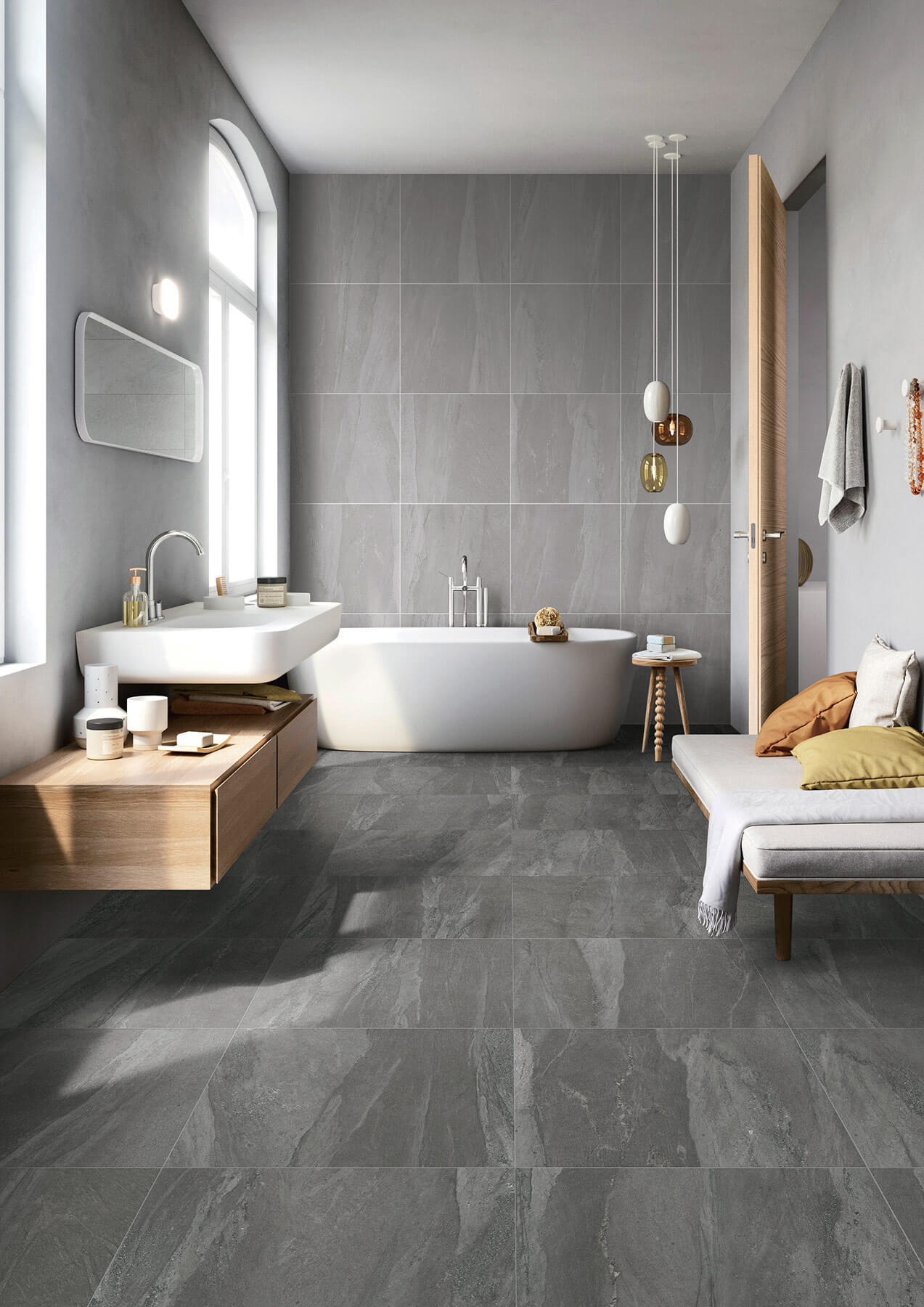 Large modern bathroom with dark grey tile floor and light grey tile walls. White soaker tub and vanity.